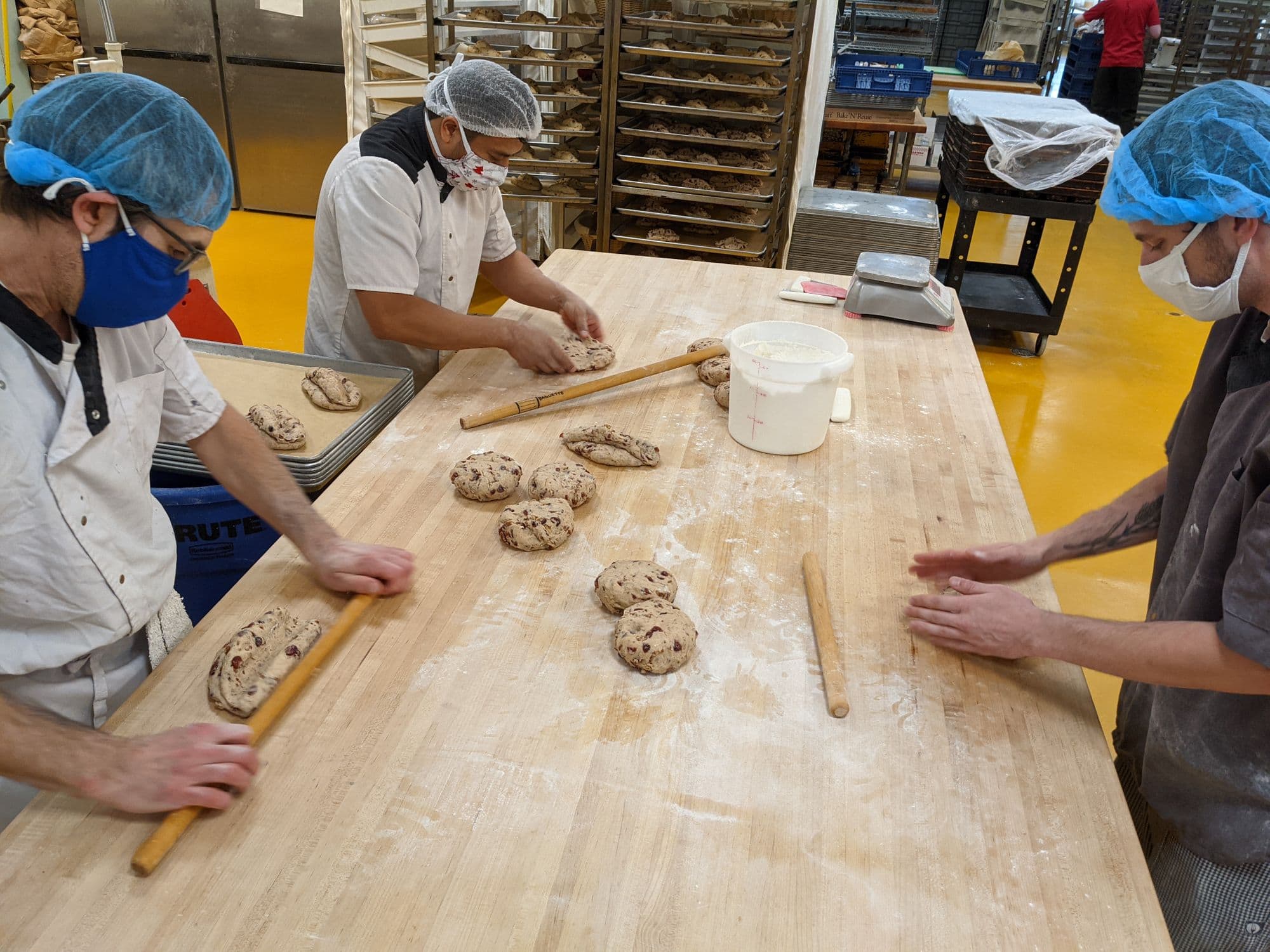 Three bakers in a bakery rolling out dough for bread