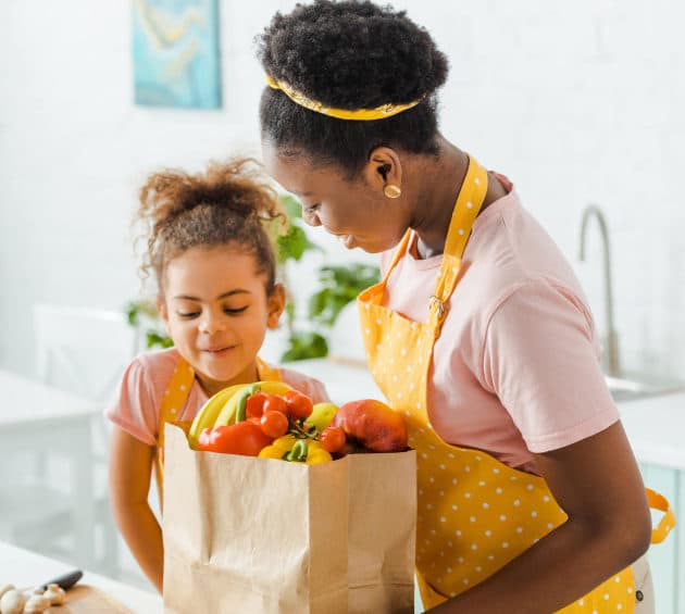 happy african american mother and daughter looking at paper bag