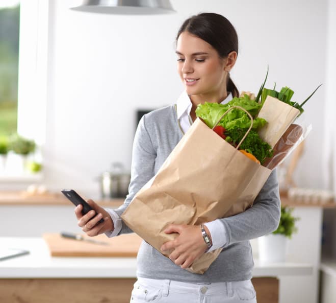 smiling-woman-with-mobile-phone-holding-shopping-bag-in-kitchen-rosie-application
